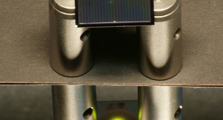 Eine zweiseitige Silicium-Solarzelle – hier aufgelegt auf Aluminium-Zylindern – wird von oben mit einem Infrarotlaser beleuchtet.